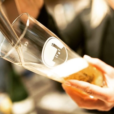 Hand hält Bierglas mit Einkornlogo wird gerade an Zapfhahn mit hellem Bier befüllt.