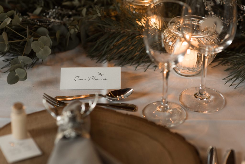 Nahaufnahme eingedeckter Tisch für Winterhochzeit mit Namensschild Oma Maria, Teelicht, Gläser und Holzplatte als Teller